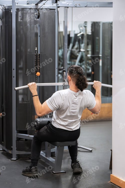 Preview: Man in focused lat pulldown workout at a gym.