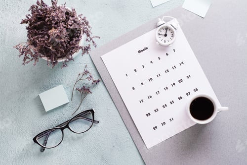 Preview: Monthly calendar sheet, coffee cup, alarm clock, glasses and a bouquet of flowers on the table.