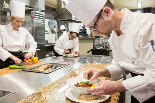 Preview: A caucasian male chef putting the finishing touches on a plate of fish in a commercial kitchen.