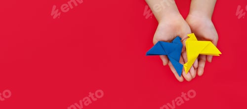 Preview: two doves origami in yellow and blue colors of Ukrainian flag in children's hands on red background