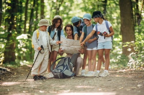 Preview: Path searching, sitting and reading a map. Woman is doing tour for group of kids in the forest