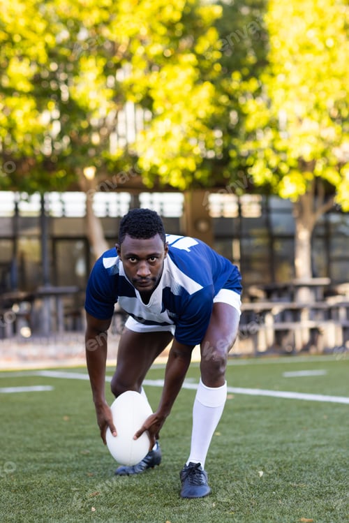 Preview: African American young male athlete placing rugby ball on field, looking focused, copy space