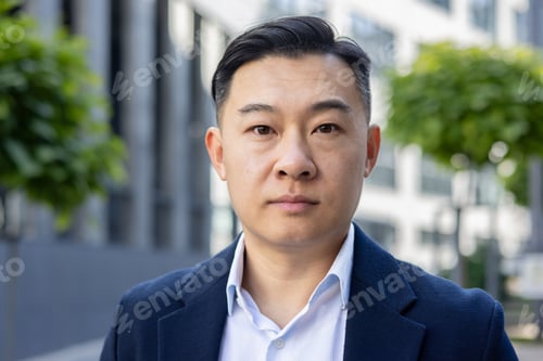 Preview: Confident asian businessman in suit posing for professional headshot outdoors
