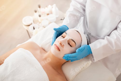 Preview: Cosmetology. Beautician doctor applying face mask to young woman in spa salon
