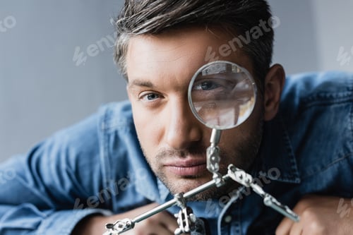 Preview: Portrait of repairman looking at camera through magnifier on blurred background