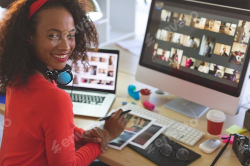 Preview: Young mixed-race female graphic designer looking and smiling at camera while working