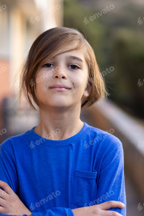 Preview: Smiling boy in blue shirt standing confidently with arms crossed outside school