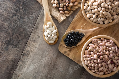 Preview: Spoons and bowls with assorted beans resting on rustic wooden table