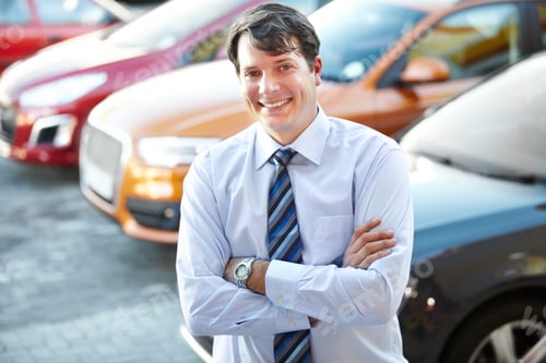 Preview: A man smiling confidently while standing in the lot of his dealership