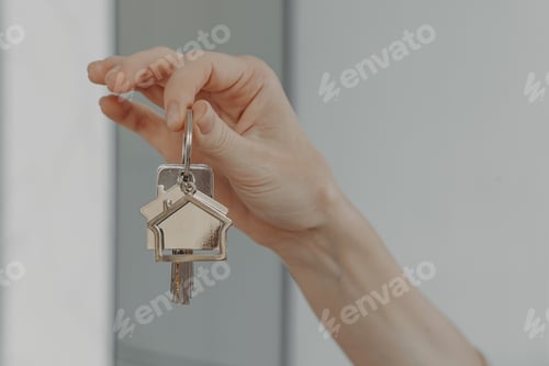 Preview: Woman holding house shaped keychain, selective focuse on female hand with key from new home