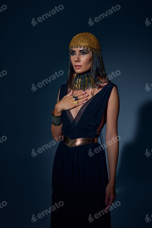 Preview: Elegant woman in egyptian headdress and necklace posing while standing on blue background