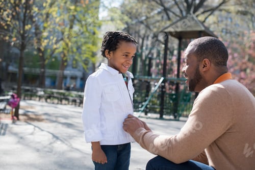 Preview: City park in Spring,Sunshine and cherry blossom. A father kneeling and buttoning his son's jacket.