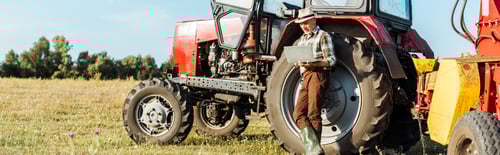 Preview: Man Using Laptop Near Tractor in Sunny Field