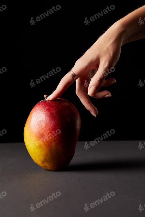 Preview: cropped image of woman touching mango on black background