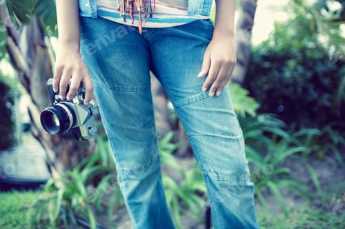 Preview: Woman wearing jeans holding camera outside on a sunny day