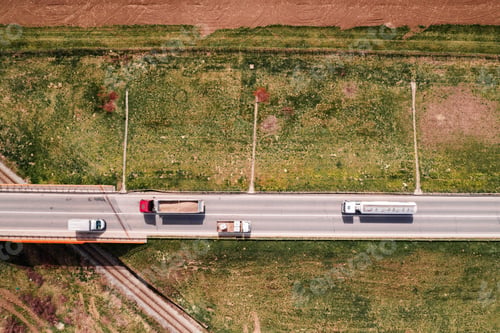 Preview: Aerial view of semi-trucks and lorries on highway with railroad overpass, directly above drone pov