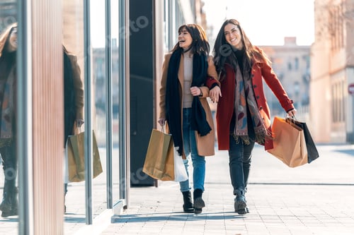 Preview: Two beautiful friends talking and having fun while walking on the city street with shopping bag.
