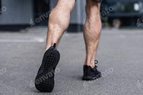 Preview: partial view of sportsman in black sneakers walking on street