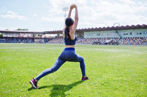 Preview: Portrait of a beautiful woman in sportswear stretching her muscles in the stadium.
