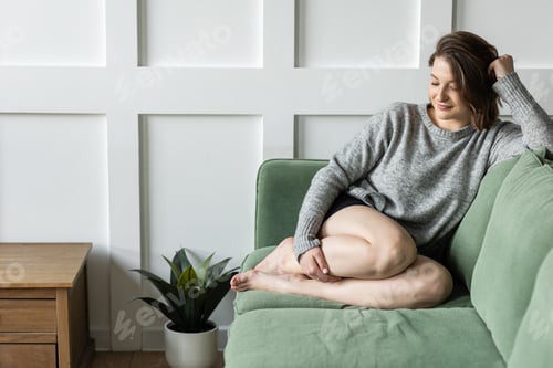 Preview: Young woman at home sitting on the green sofa. Feeling relaxed and happy