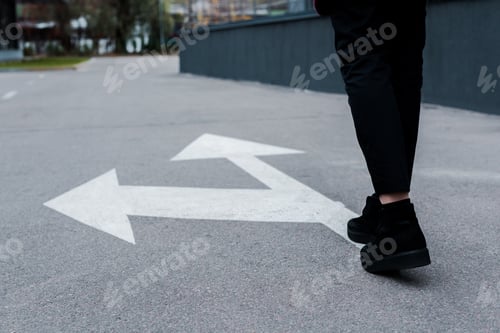 Preview: cropped view of woman walking near directional arrows on asphalt