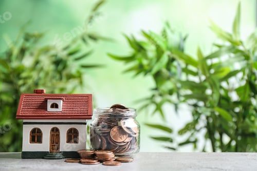 Preview: House model and jar with coins on table against blurred background. Space for text