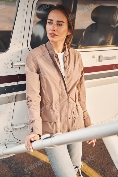 Preview: Woman in Jacket Leaning Against Small Airplane
