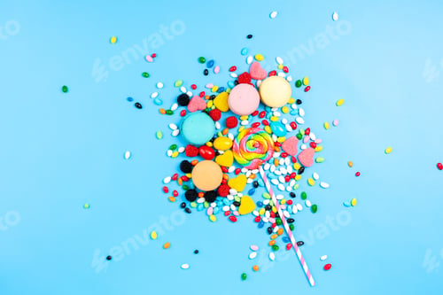 Preview: a top view multicolored candies along with colorful french macarons spread all over the blue