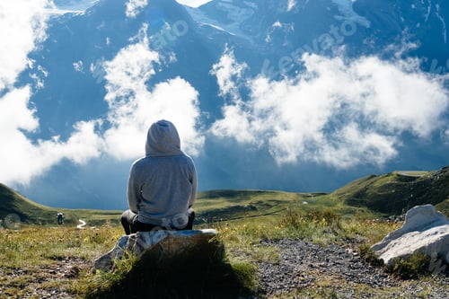 Preview: Young woman sitting looking at sea of clouds in mountain landscape