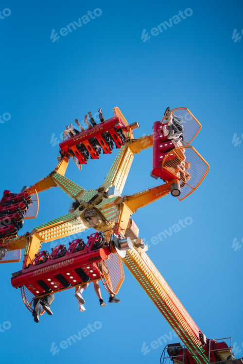 Preview: View from below of people enjoying a high-thrill amusement ride at a fair, with a clear blue sky