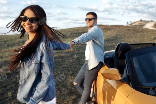 Preview: Stylish young couple staying beside a yellow convertible car. Freedom, travel and love concept.