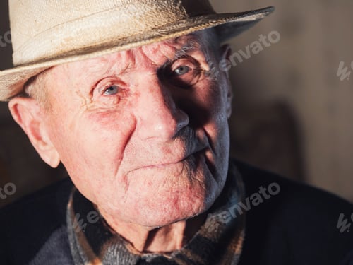 Preview: portrait of 92 years aged senior caucasian man with white hat looking at camera against white wall
