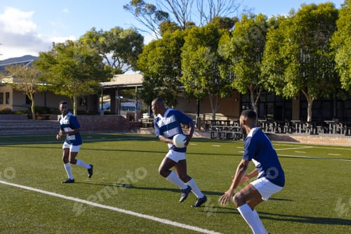 Preview: Three African American young male athletes wearing sportswear are playing rugby on field outdoors