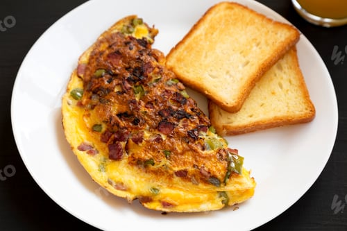 Preview: Homemade Denver Omelette on a white plate on a black background, side view.