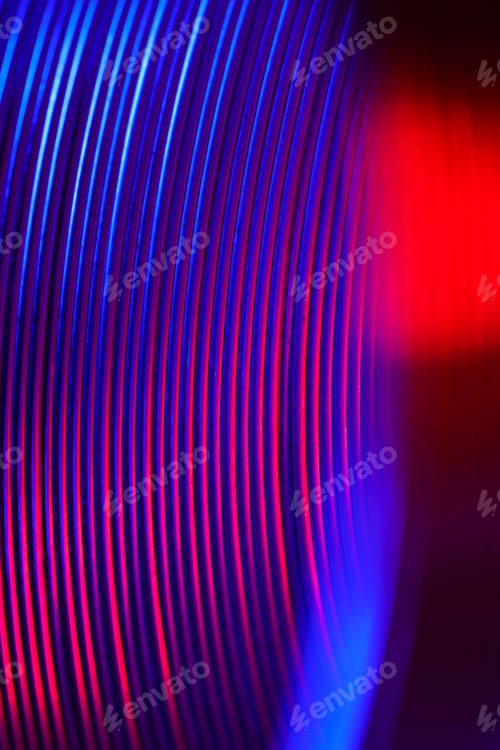 Preview: Closeup of coiled metal spring rings in a compressed state in red and neon light, macro photo