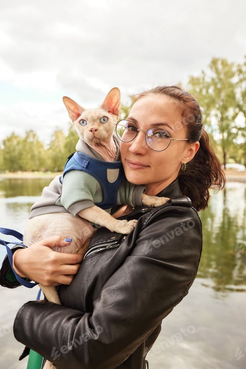Preview: The young woman is holding her cat in amoveralls on her feet. Cat on a walk. Love to the animals