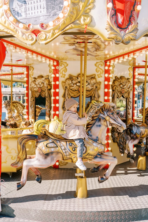 Preview: Little girl rides a toy horse on a colorful carousel in a sunny square