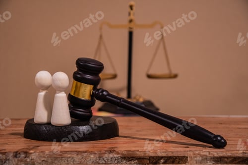 Preview: A judge's gavel and scales of justice stand next to two wooden figures. judicial