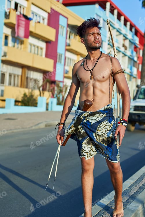 Preview: Tribal man with his traditional arch and arrows in the middle of the city with cars passing by, Luba