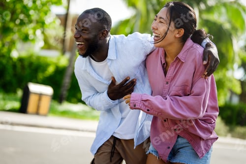 Preview: Happy interracial couple laughing together outdoors, enjoying a carefree moment of love, joy