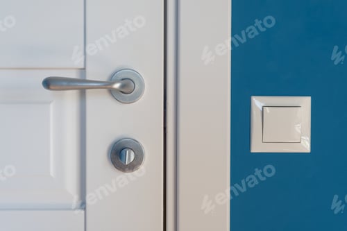 Preview: Detail of a white interior door with a chrome door handle and latch, light switch on the wall.