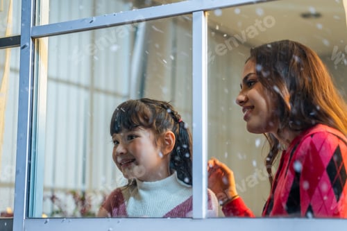 Preview: Adorable child looking at the window and admire snowflakes with mother.