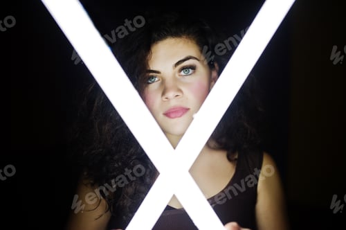 Preview: Curly brunette plus size model with two long led lamp at black room.