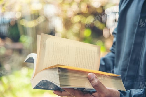 Preview: Asian man holding book reading magazine at green park in natural garden. man relax read open book