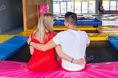 Preview: Man and woman sits together on a trampoline indoors.