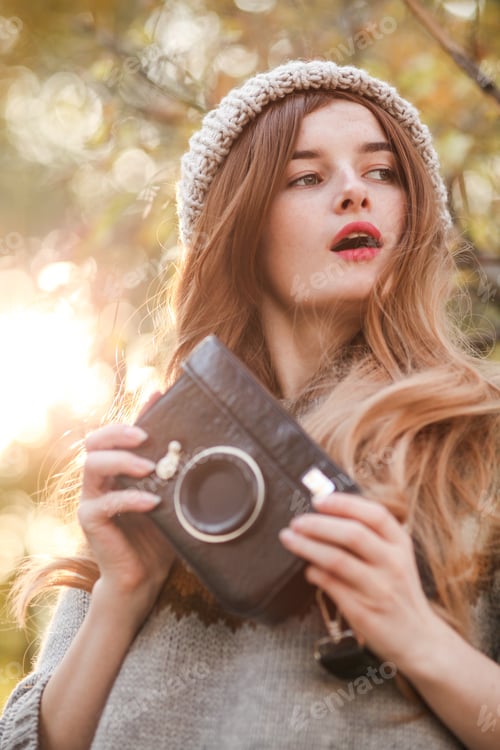 Preview: Young woman holding a vintage old camera. She's wearing warm clothes in winter or fall