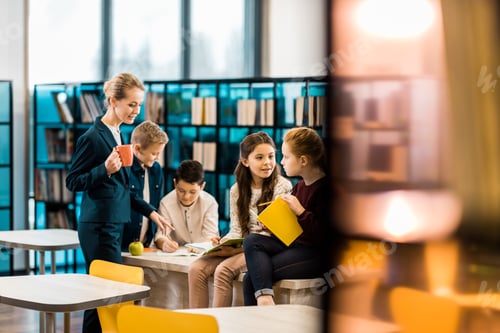 Preview: selective focus of schoolchildren and librarian talking together in library