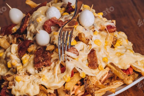 Preview: Closeup shot of a dish with french fries, sausages topped with cheese and corn on a wooden table.
