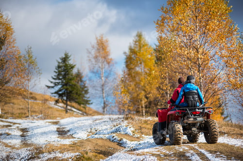 Preview: Two female riders ATV on a snow-covered trail at sunny autumn day against mountains.