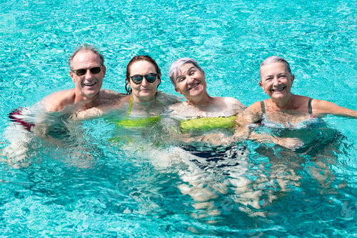 Preview: Group of four cheerful relaxed friends having fun in outdoor swimming pool under the sun